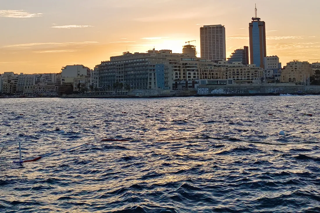 The Sliema seafront at sunset seen from the water, with the towers of the promenade behind