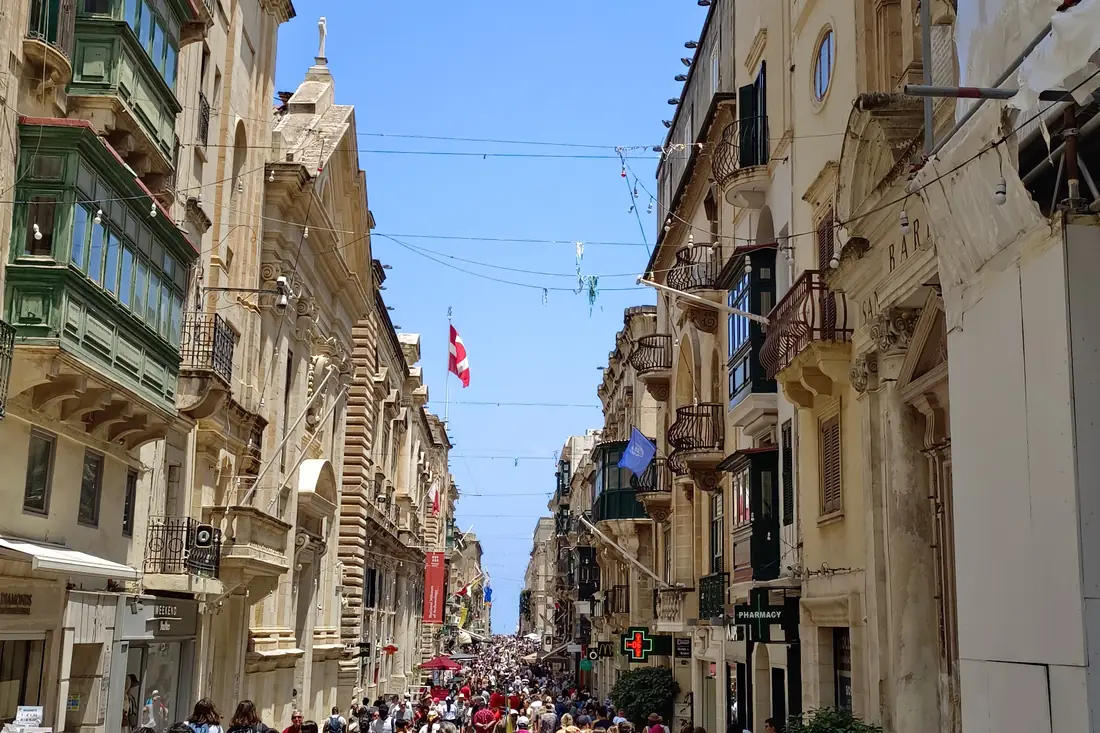 Republic Street in Valletta on a summer afternoon, crowded, with enclosed wooden balconies on both sides