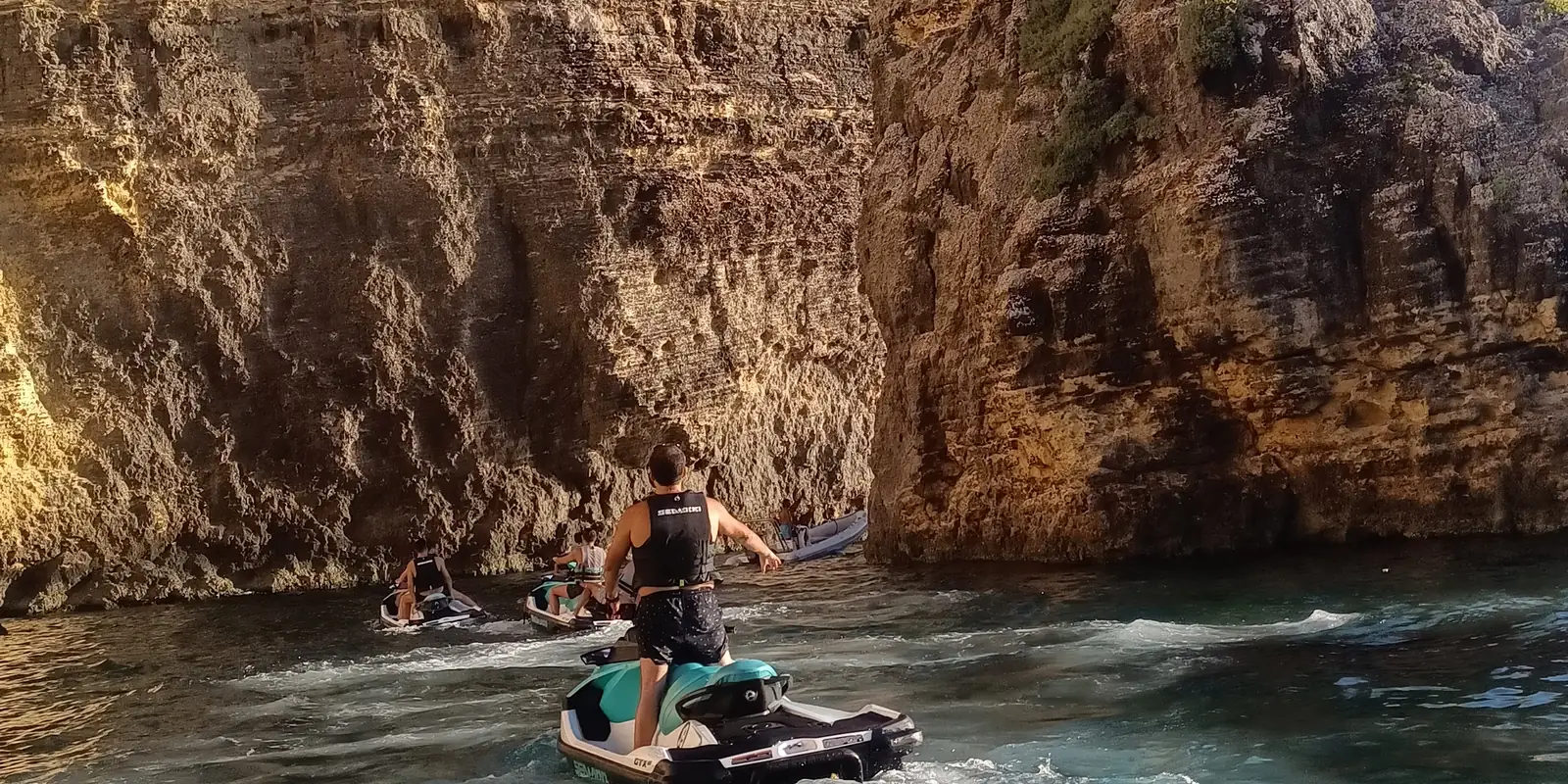 The limestone cliffs of Comino above clear water, with jet skis passing below