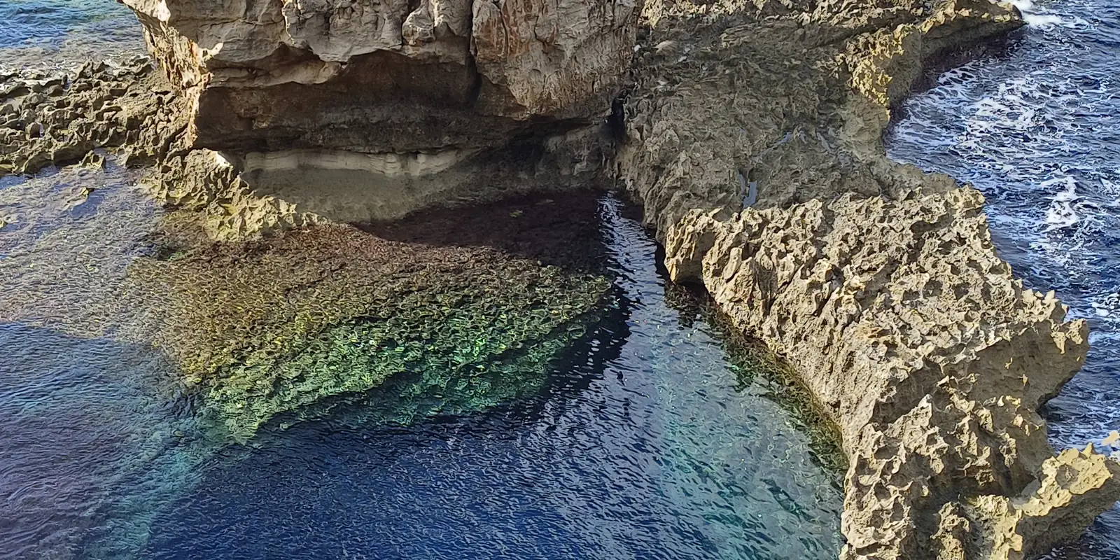 A natural rock pool cut into the Maltese coastline with waves breaking beyond