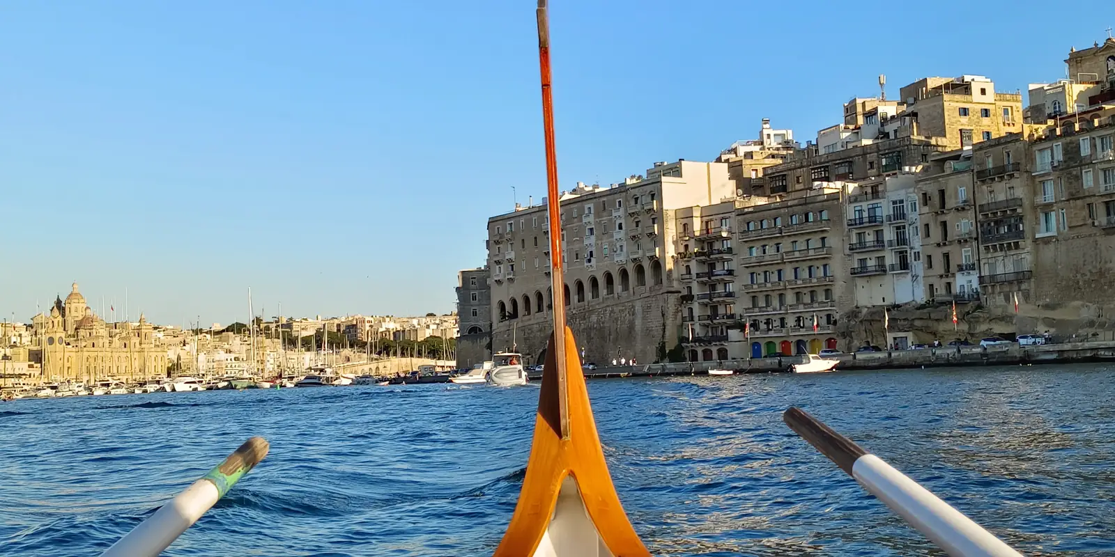 A traditional Maltese boat crossing the Grand Harbour towards the houses of Senglea