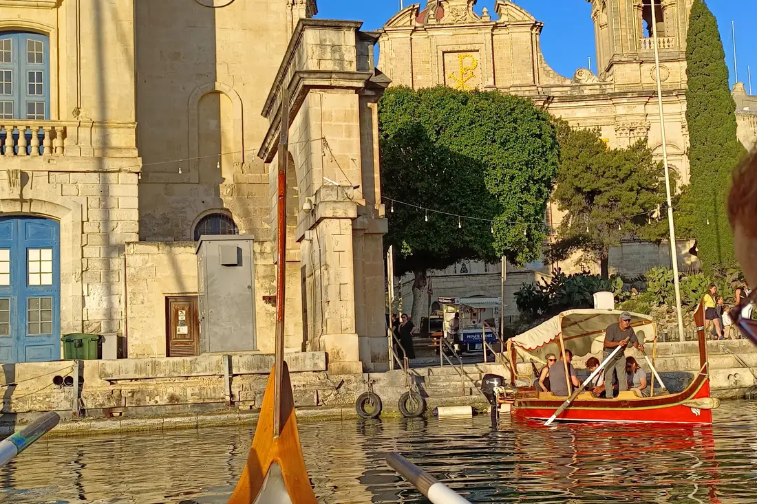 A traditional Maltese dghajsa boat crossing the Grand Harbour at Birgu in evening light